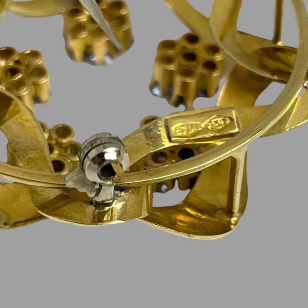 Close up photo of the hallmark on the back of gold blue topaz brooch. The silver coloured metal clasp is seen next to hallmark.