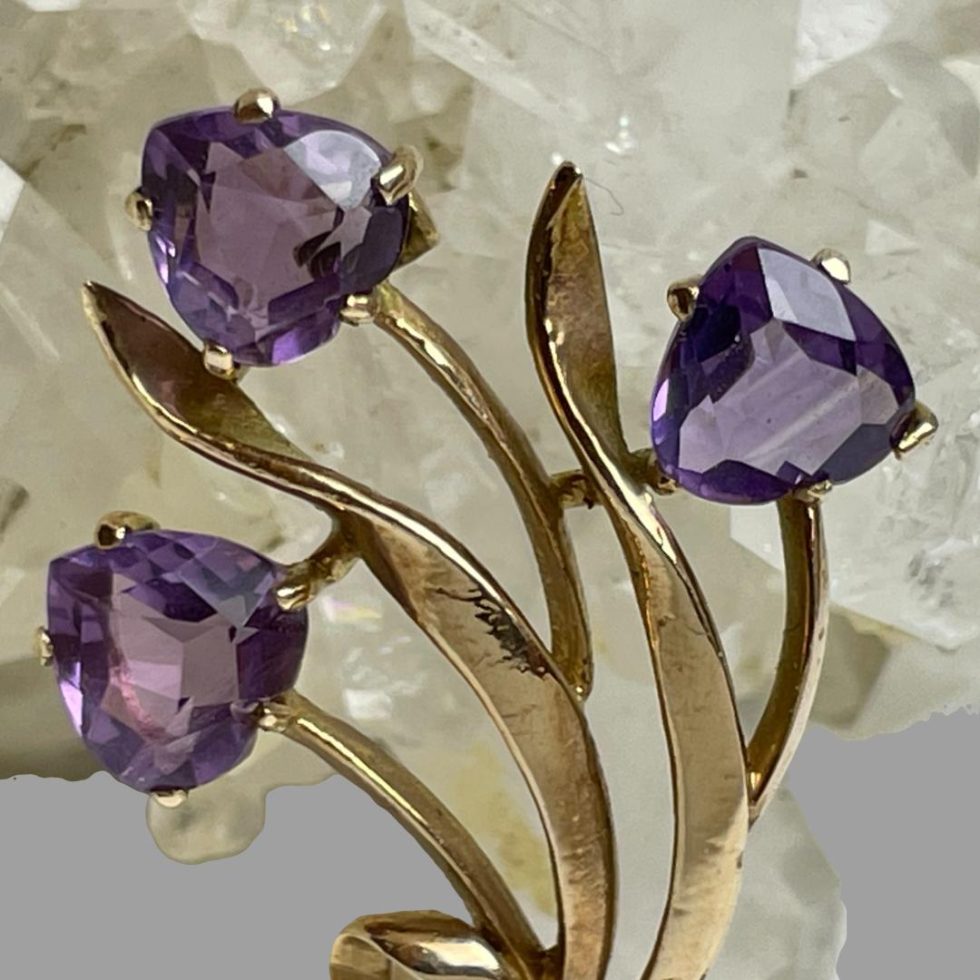 A close up photo of the flower heads of this gold amethyst tulip brooch still leaning against natural quartz crystal.