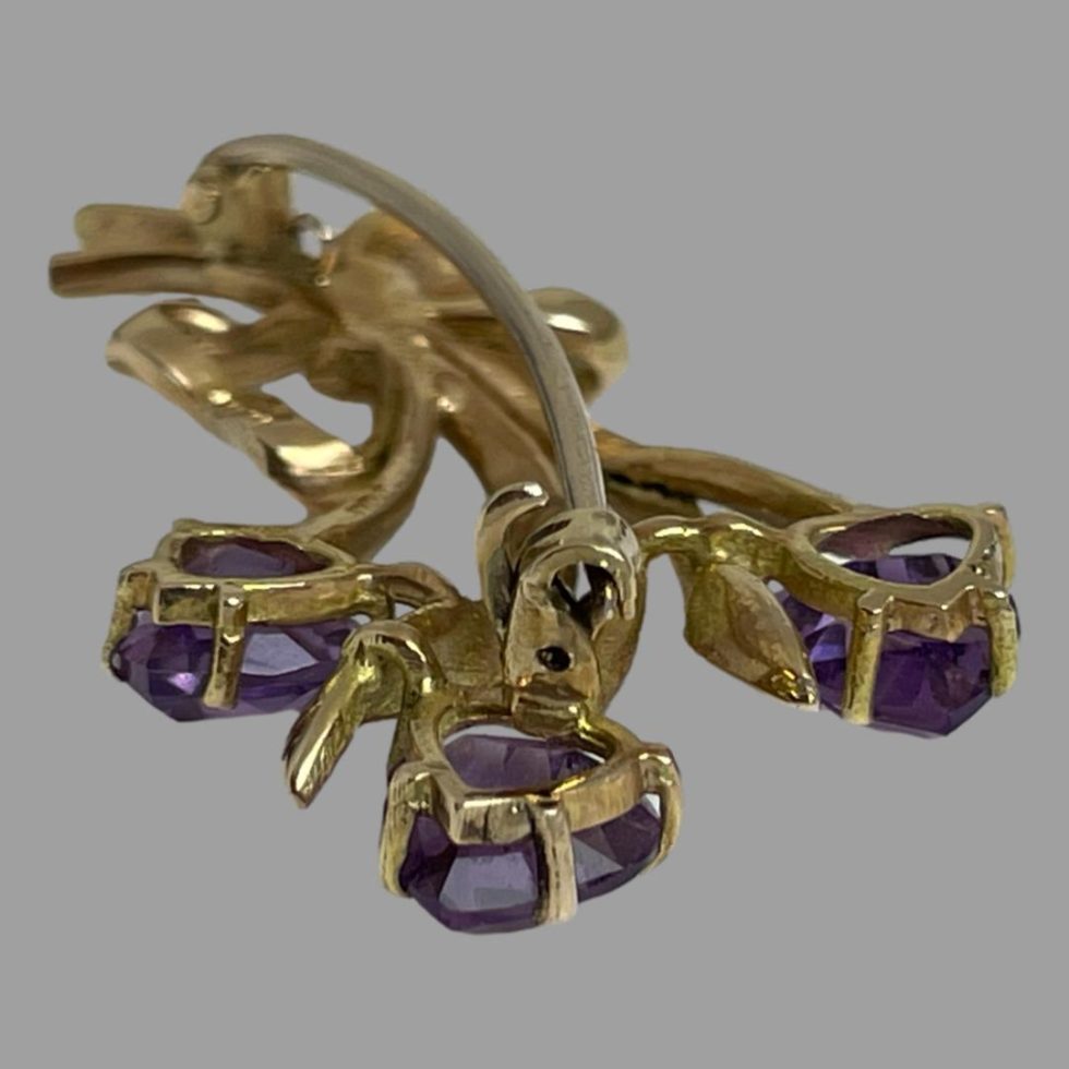Photo of gold tulip flower brooch displayed face down on a flat surface with the flower heads end in the foreground to show the clever curved design of the pin and the hook lock clasp mechanism. The upper hook is shown open.
