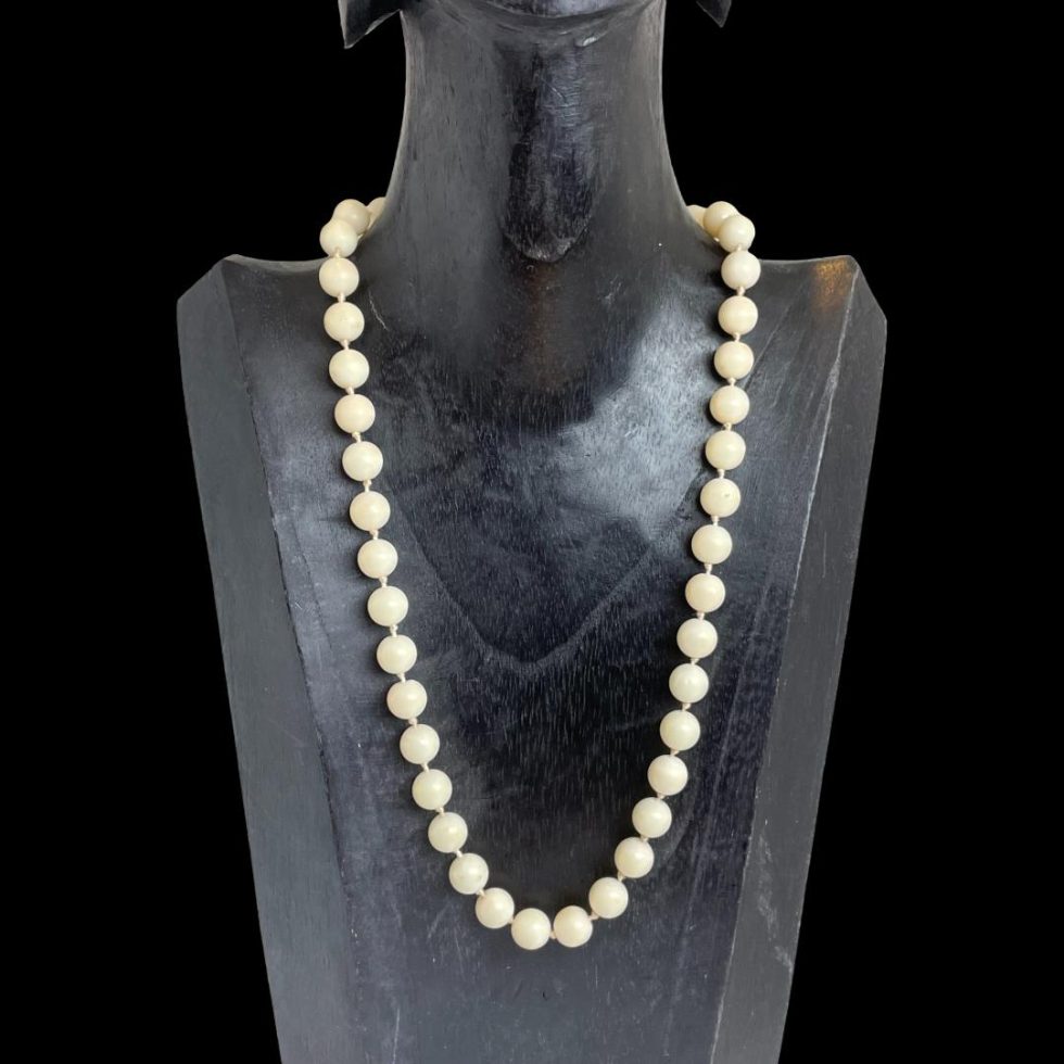 Photo of antique white coral necklace displayed on a dark wood display stand with the uniform white coral beads only displayed.