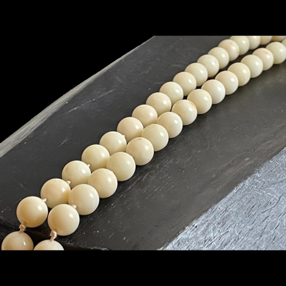 Photo of antique white coral necklace displaying strung beads side by side so looks like 2 rows. The natural colour of the coral is visible and some of the hand knotting between each bead.