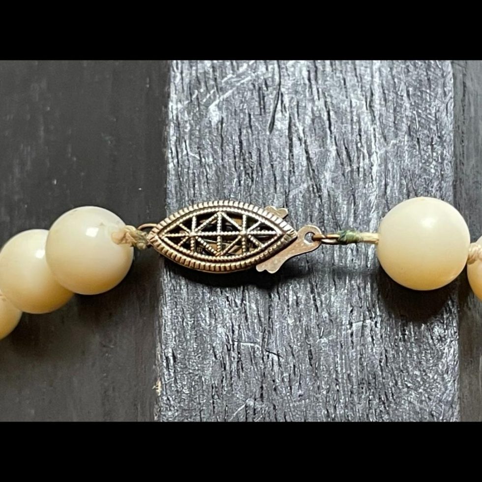 Close up photo of the clasp area of antique white coral necklace. The clasp is metal possibly with copper included and is of an intricate pierced design. It is an old school clasp with a hook that pushes into the cover and clicks shut.