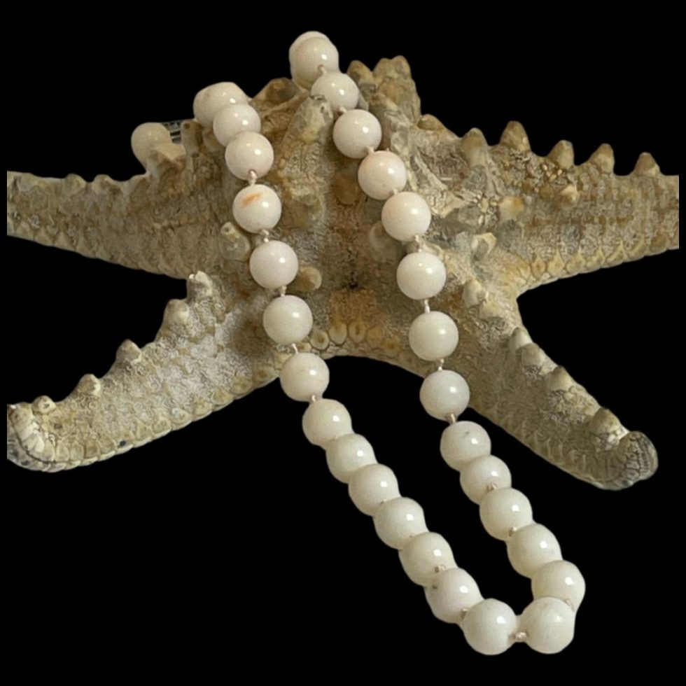 Main photo of antique white coral necklace displayed draped over a starfish. The coral beads are a lovely natural white with small flecks of pale pink and the knotting between each bead is visible.