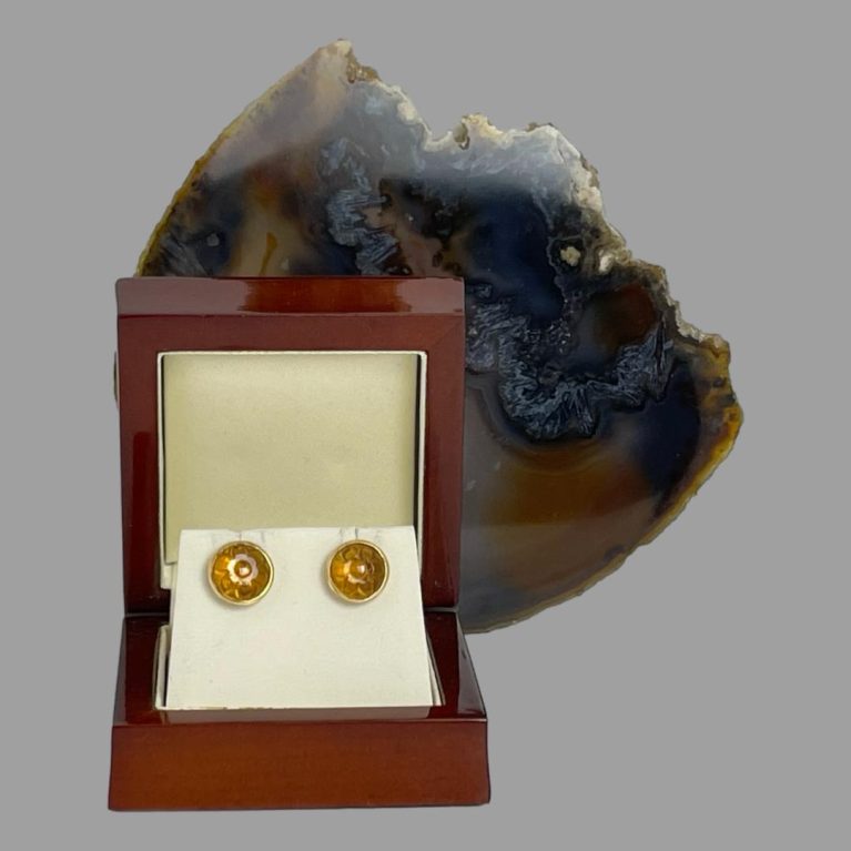 Main photo of carved citrine gold earrings displayed inside their lacquer wood box. There is a slice of natural agate behind the open box.