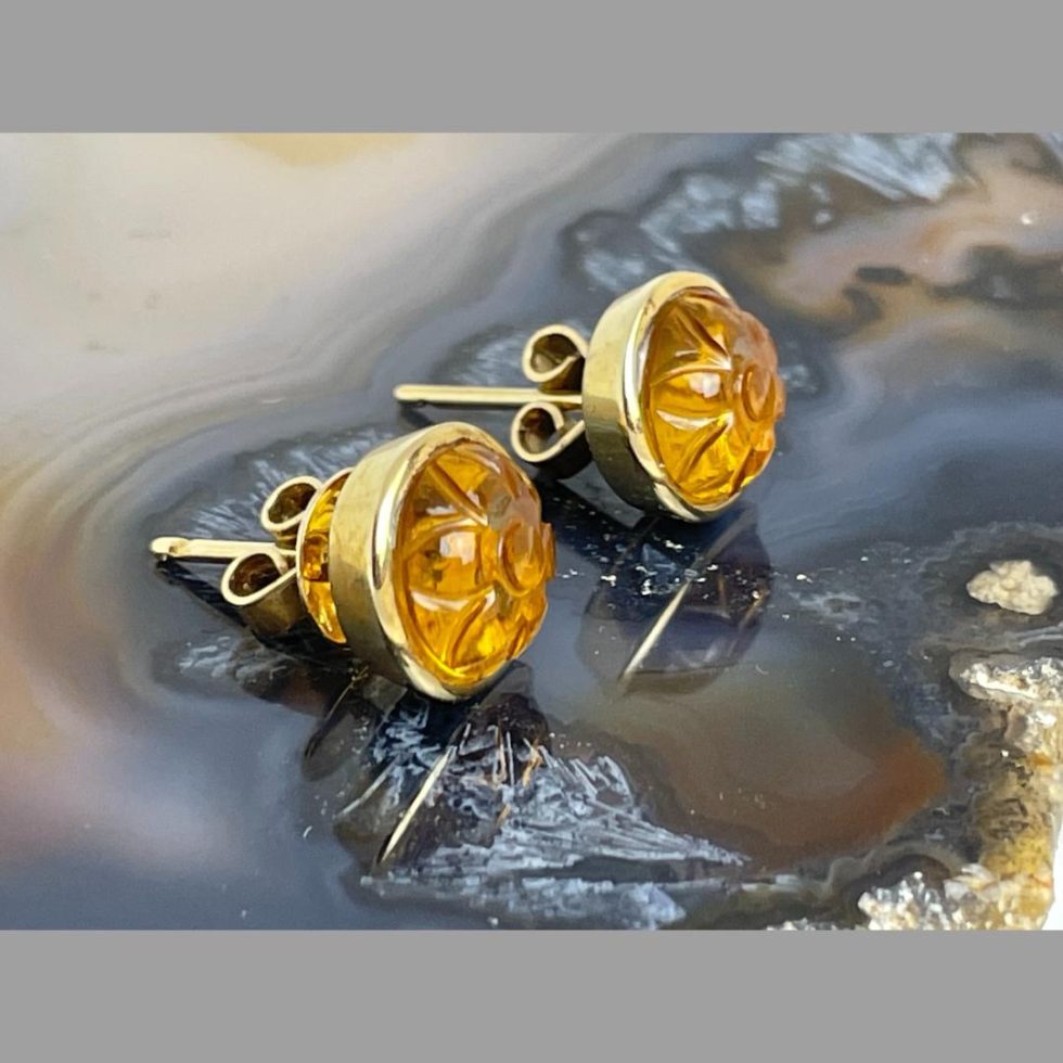 Photo of both carved citrine gold earrings on top of some agate and shown from a side angle with the earring fronts faced towards the right.