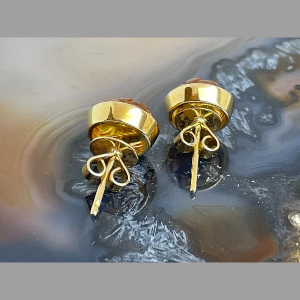 Photo of carved citrine gold earrings displayed on top of a slice of natural agate and seen with the back ends on show with their butterfly fasteners in place.
