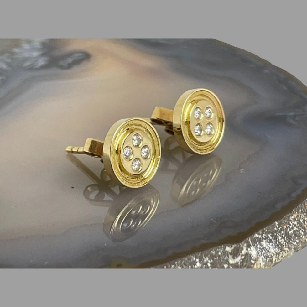 Main photo of gold diamond 'button' earrings displayed on top of a slice of natural agate and seen with the front of earrings facing towards the right. The 'button' detail is very clear - button like a shirt button; round with 4 thread holes. The diamonds making the thread holes have a lovely sparkle.