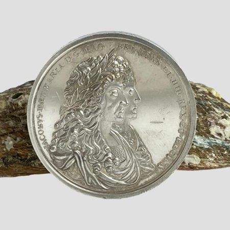 Main photo of reproduction silver commemorative medal showing the obverse conjoined busts of James II and Mary. The medal is leant against a piece of abalone shell.