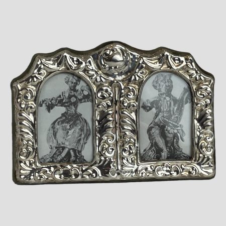 Main photo of small double photo frame seen forward facing. The sterling silver frame around the front of the frame is elaborately decorated with embossed detail. The area for the photos are small with an arched top.