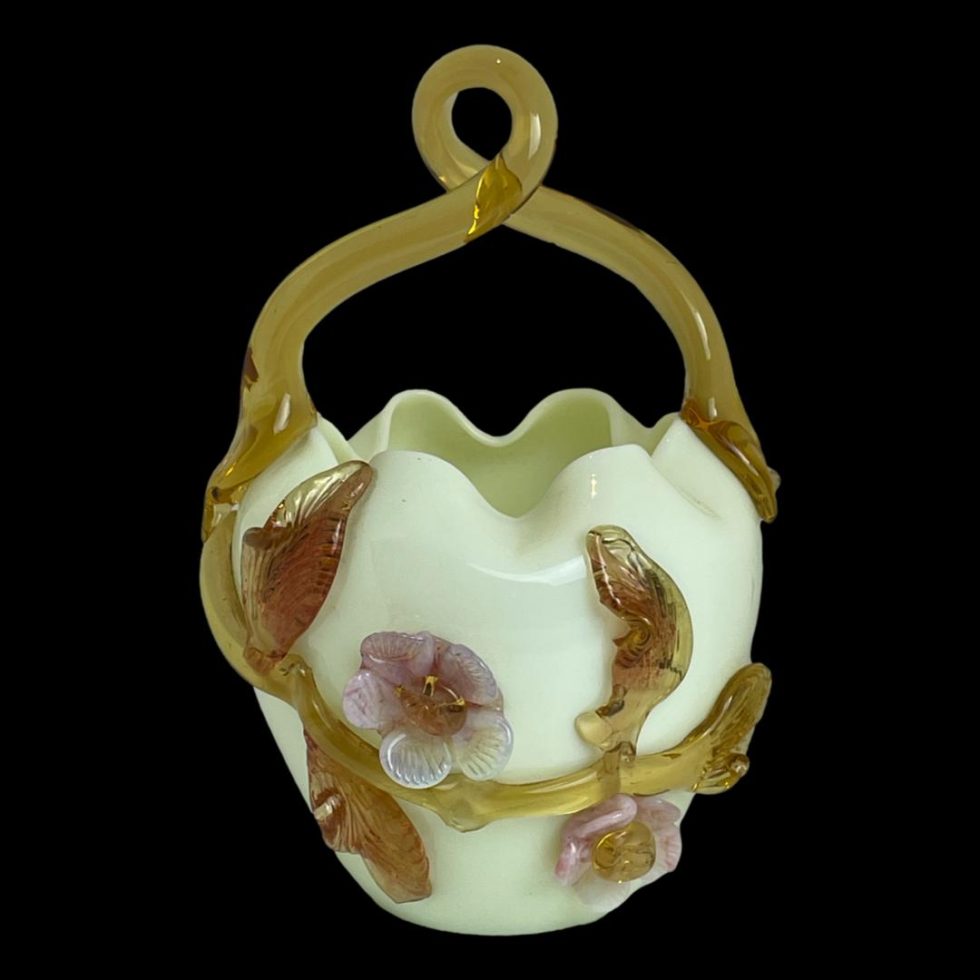 Main photo of Victorian uranium glass basket seen from the side decorated with pink glass flowers and butterscotch glass leaves, stalks and handles. The handle appears to be part of the foliage like a vine stalk. The uranium glass is the actual basket which could appear like the lower half of a hard boiled egg. The colour could be described as milky minty yellow. The wonderful thing about this item is that whilst this side is decorated with flowers, the opposite side is without decoration so on your 'no bling' days you can opt for egg shell.