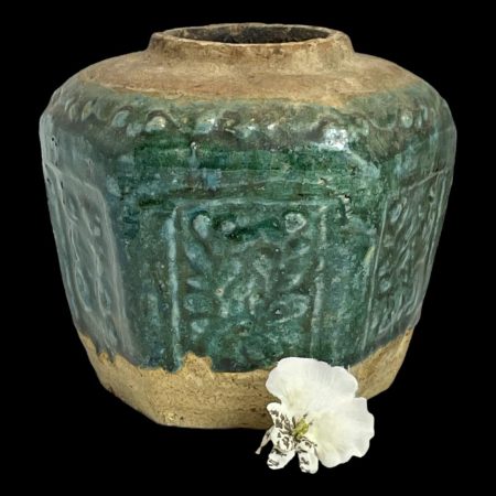 Main photo of 19th century ginger jar seen almost from an eye level. The top of the jar and base area are natural stoneware pottery whilst the central area is a beautiful shade of green called shiwan which is like a dark forest green with a hint of jade.3 of the 6 sides are on display. There is a foliage theme to the decoration on the 6 sides of the pot under the green glaze. A single white orchid is displayed just off centre to the bottom right.