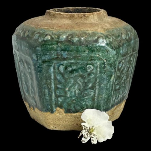 Main photo of 19th century ginger jar seen almost from an eye level. The top of the jar and base area are natural stoneware pottery whilst the central area is a beautiful shade of green called shiwan which is like a dark forest green with a hint of jade.3 of the 6 sides are on display. There is a foliage theme to the decoration on the 6 sides of the pot under the green glaze. A single white orchid is displayed just off centre to the bottom right.