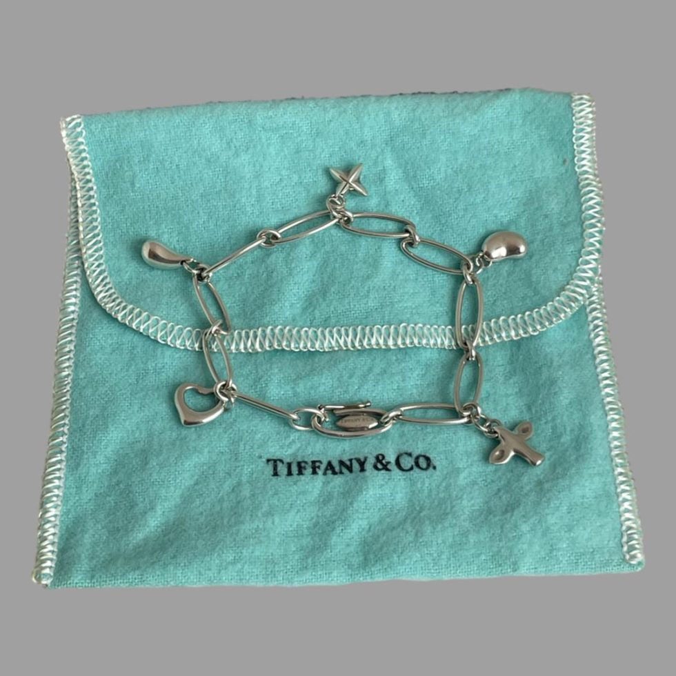 Photo of Elsa Peretti Tiffany bracelet displayed in full on top of the iconic turquoise coloured Tiffany & Co pouch. The bracelet is laid in a circle with the charms out spread
