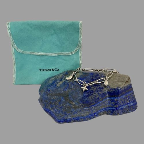 Main photo of Elsa Peretti Tiffany bracelet displayed on top of a rock of natural blue lapis lazuli with the turquoise blue Tiffany & Co pouch upright to the back left. The image evokes a sense of sun & sea & Spain ole !