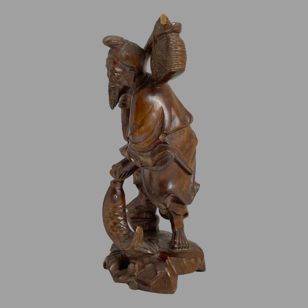 Photo of carved wooden Oriental fisherman seen this time with the carp in the foreground to the left and the fisherman looking towards the left.
