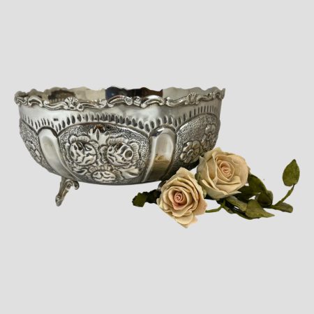 Main photo of 835 Continental silver bowl seen from an eye level. The main side on display shows rosehips in the panel and to its left there are dog roses in bloom. The rim has a lovely wavy patterned edge and the tripod feet are a triangular shape with the ends tapering to a near point. A small posy of pink roses sits to the bottom of right of bowl.
