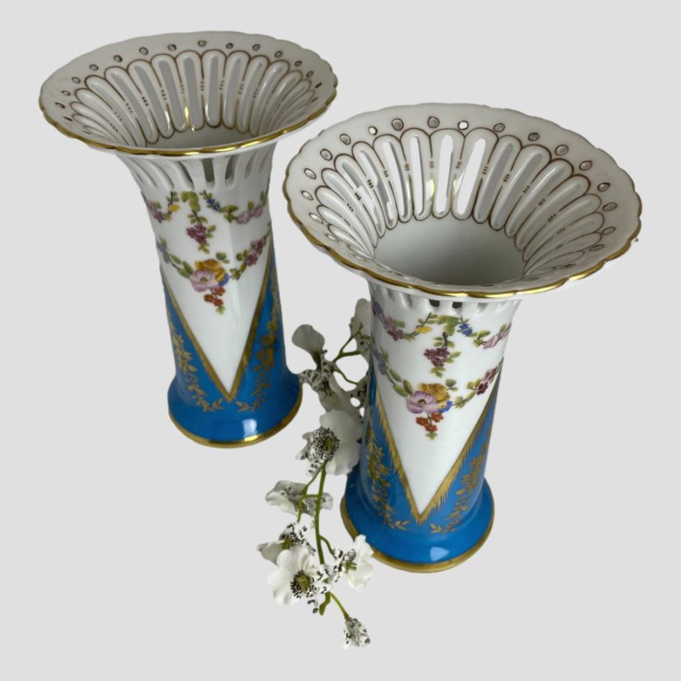 Photo of Sêvres style porcelain vases this time seen from a little raised angle looking diagonally down with the flared pierced tops visible. The spray of white orchids is still placed between the 2 vases.