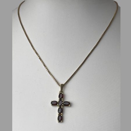 Main photo of gold garnet cross & chain displayed on a stand and seen with front of cross facing forward. The chain is a box chain of good thickness. The pendant has a smooth bail with 4 oval cut garnets going down and an oval cut garnet horizontally for the arms on the left and right so total of 6 garnets. Each garnet is held in place with 4 prongs so a nice secure setting.