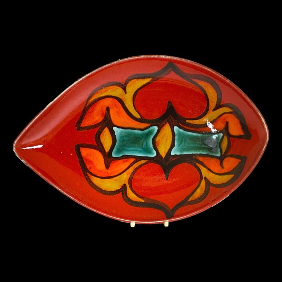Main photo of red Poole Delphis dish seen displayed on a plate stand looking at the brightly coloured decorated interior of dish. The longer pointed end is to the left.