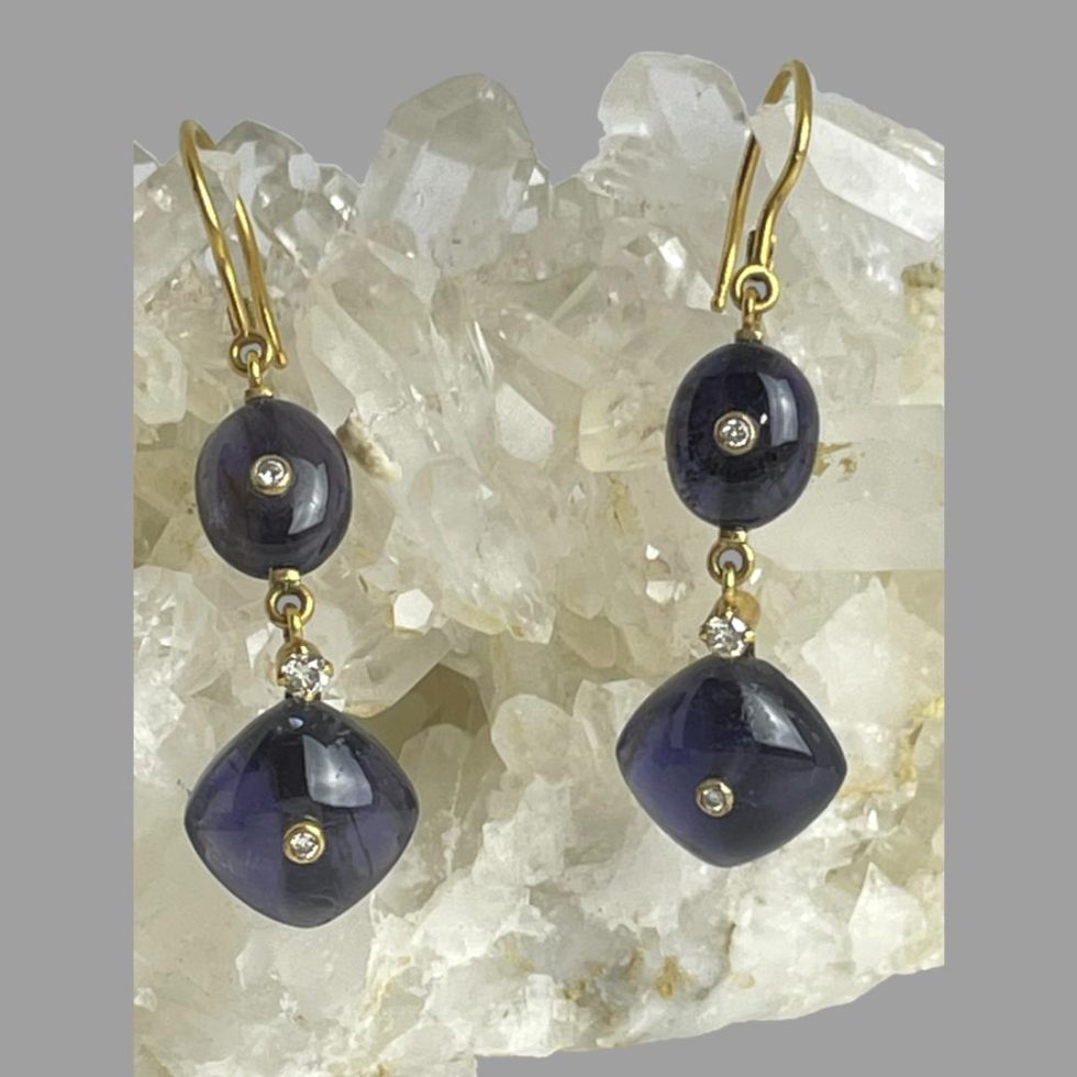 A close up photo of the gold iolite diamond earrings still displayed hanging from a rock of natural quartz crystal.