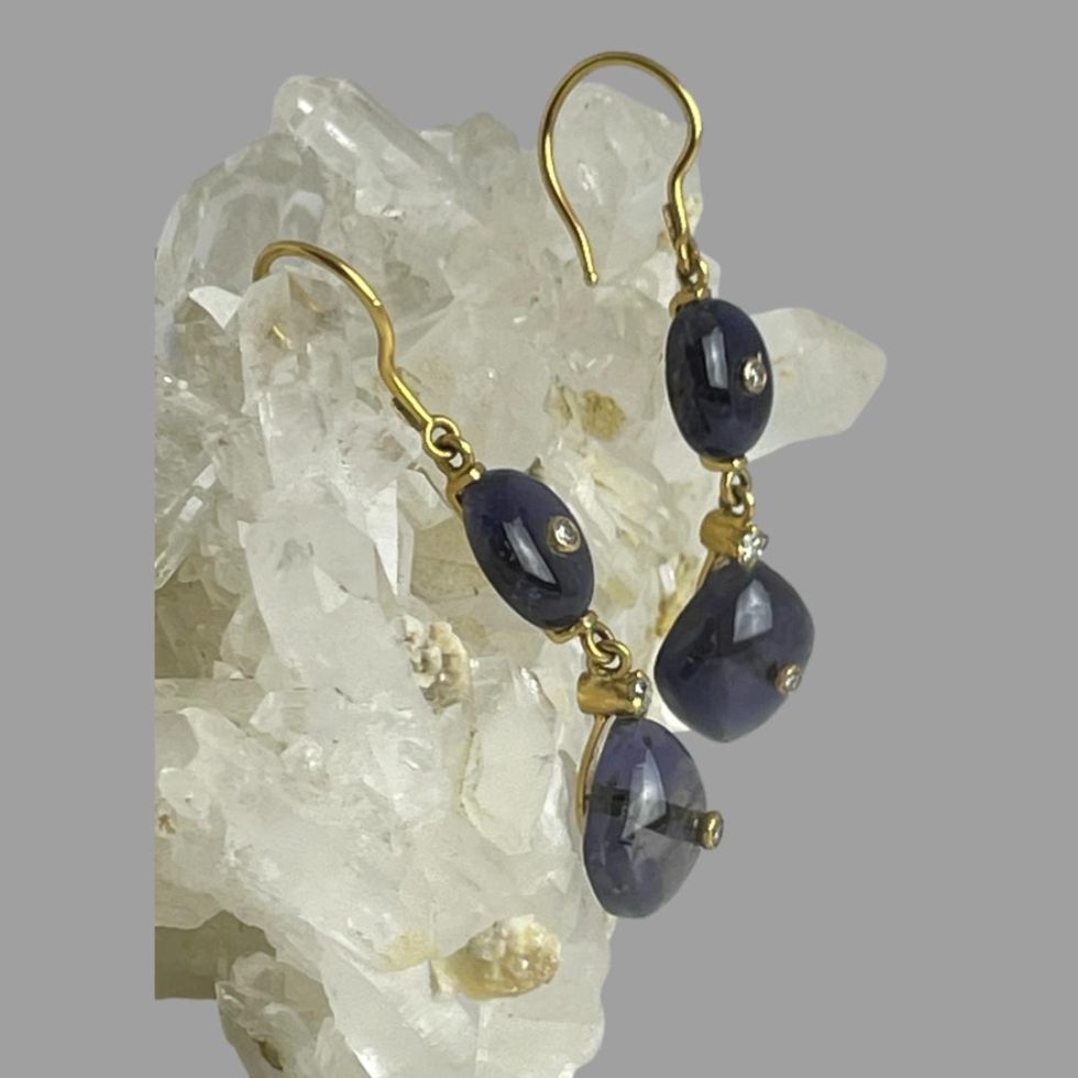 Photo of gold iolite diamond earrings shown displayed hanging from a rock of natural quartz crystal and from a side angle with the front of earrings facing right.