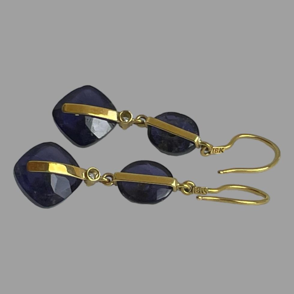 The gold iolite diamond earrings are displayed vertically on a flat surface and face down showing the construction setting.