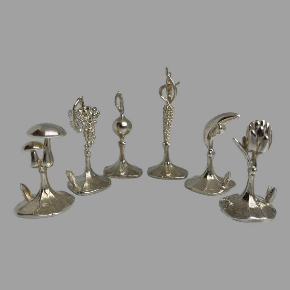 Photo of Italian name card holders displayed in a curved row with from Left to Right mushroom, grapes, turnip, corn on the cob, banana (one bit of skin peeled halfway) and globe artichoke.
