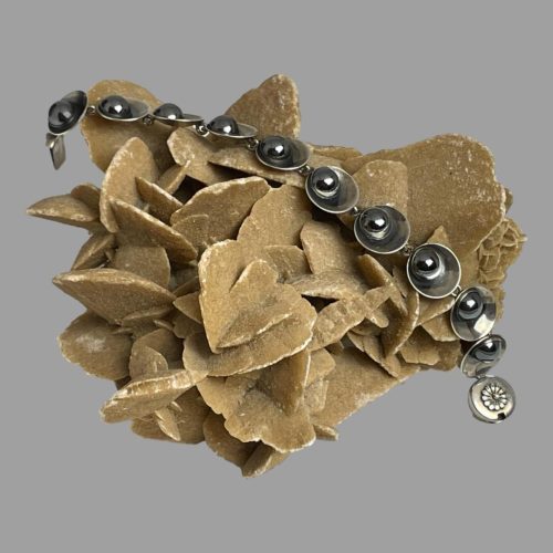 Main photo of Modernist Danish silver bracelet shown unclasped and displayed across a rock of natural desert rose. The circular housing for the clasp is in the bottom right corner with other end of bracelet in top left corner. More detail of bracelet design on close up photo in next image