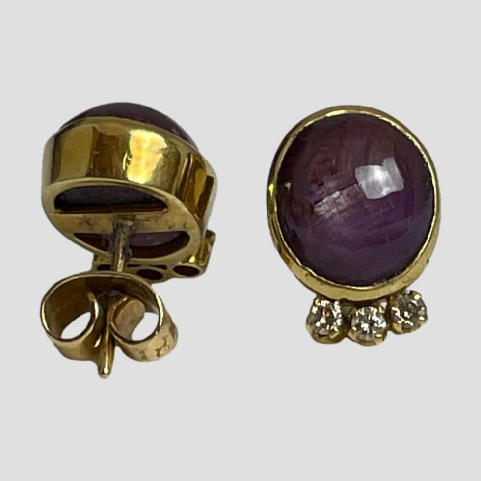 Photo of star ruby and diamond earrings laid on a flat surface with one earring forward facing and other showing the back. The earrings have a nice sturdy pair of butterfly fasteners.