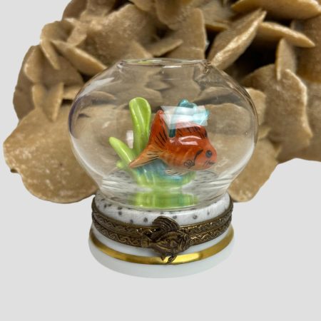 Main photo of Limoges goldfish bowl box with the goldfish in the foreground in the bowl. The goldfish is an orange/red colour with head to the right and tail on left and stands out well against the blue and green of the seaweed behind it. There is a rock of desert sand rose in the background offering an underwater 'coral' like look.