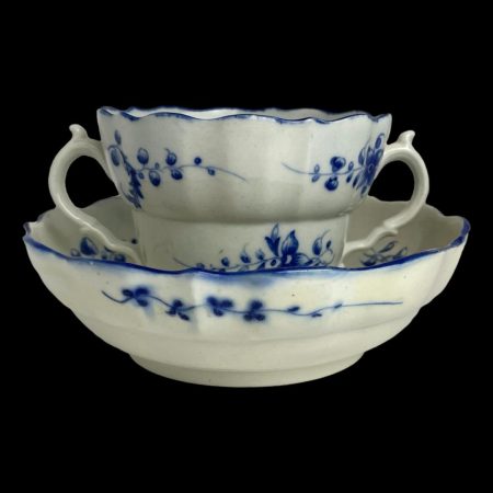 Main photo of Caughley chocolate cup & saucer seen from an eye level with the cup sat on the saucer. The saucer is more like a shallow bowl. The cup has 2 handles either side - perfect for savouring a delicious cup of chocolat chaud! Both pieces are mostly in off white with pretty blue garlands dotted here and there and blue rims. Set against a black background, these pieces are very striking.