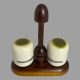 Main photo of Alvar Aalto salt and pepper seen nearly from an eye level - just slightly raised to show the matcha green coloured tops. The pots are situated in their slots on the stand. The handle for the stand is at the centre & looks like an unopened chocolate mushroom while the salt and pepper pots are like white chocolate with matcha powder glaze tops.