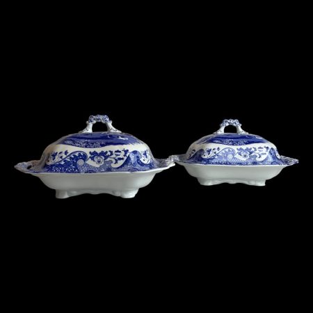 Main photo of pair Spode Italian tureens displayed almost side by side with one slightly in front of other and shown from an eye level. the lower half of tureen exterior is a plain white while the lid shows the Italian design theme. From this angle it is possible to see that the lid has more depth than the bottom part so good for piling up the vegetables!