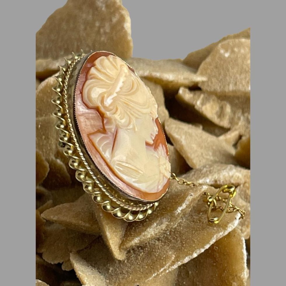 Photo of 9 karat gold cameo brooch displayed on a rock of desert sand rose and seen from a side view with the brooch front faced to the right.
