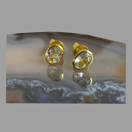 Main photo of gilt silver aquamarine studs displayed on top of a slice of natural agate with the earring fronts forward facing. The subtle blue of the aquamarines shine through with the gilt silver complimenting the look.