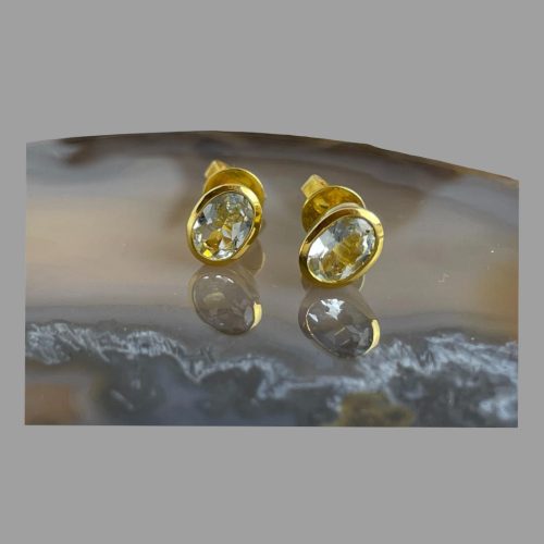 Main photo of gilt silver aquamarine studs displayed on top of a slice of natural agate with the earring fronts forward facing. The subtle blue of the aquamarines shine through with the gilt silver complimenting the look.