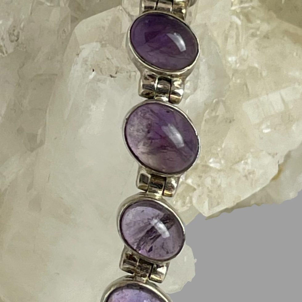 A close up photo of some of the amethyst stone links on the sterling silver amethyst bracelet which is still displayed on top of the quartz crystal rock.
