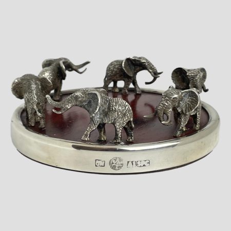 Main photo of elephants wine bottle coaster seen from an almost eye level. The 6 elephants appear to be walking around half with raised trunks. The silver plate hallmark is visible in the foreground.