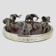 Main photo of elephants wine bottle coaster seen from an almost eye level. The 6 elephants appear to be walking around half with raised trunks. The silver plate hallmark is visible in the foreground.