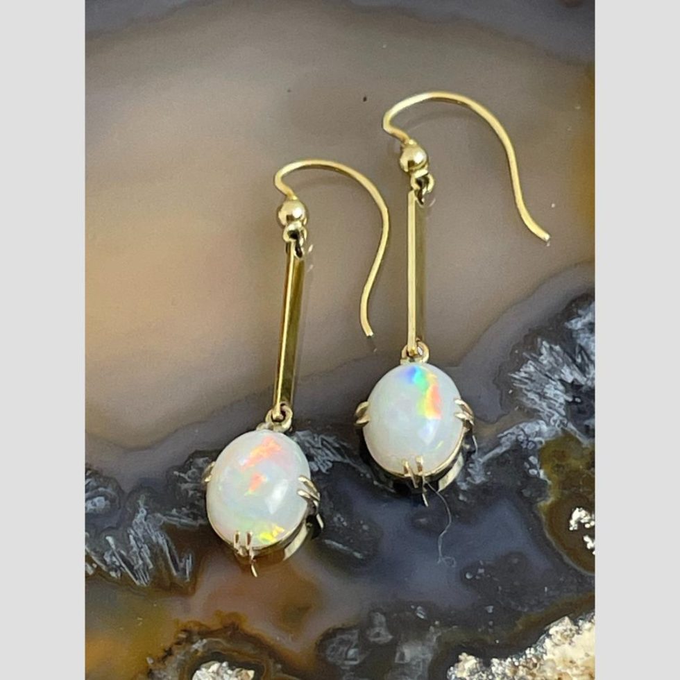 Photo of antique gold opal earrings displayed laid flat on a slice of natural agate with the opals to the centre bottom and hooks at centre top.