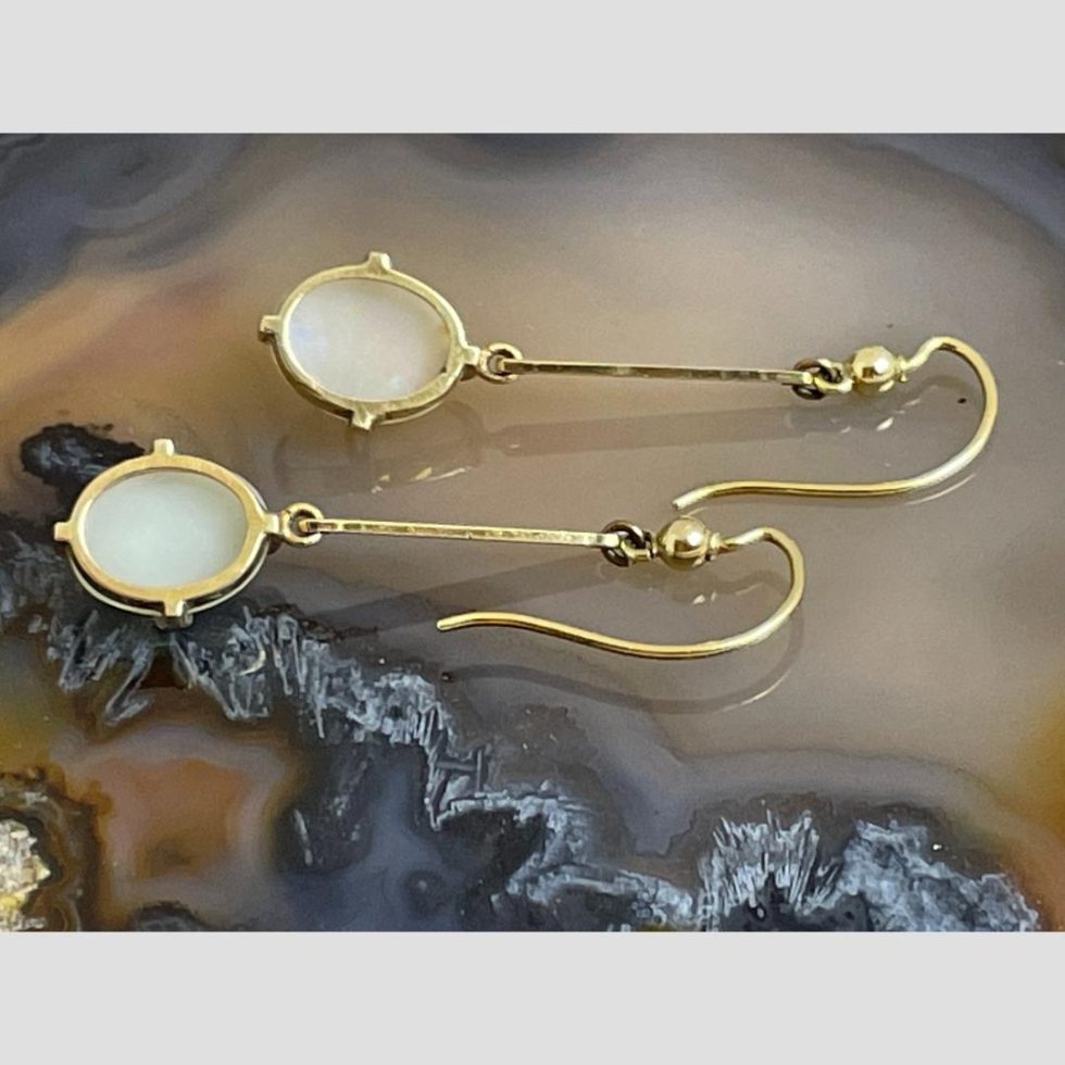 Photo of the back of both antique gold opal earrings laid flat on top of a slice of natural agate. The hooks are on the right with the opals on the left.
