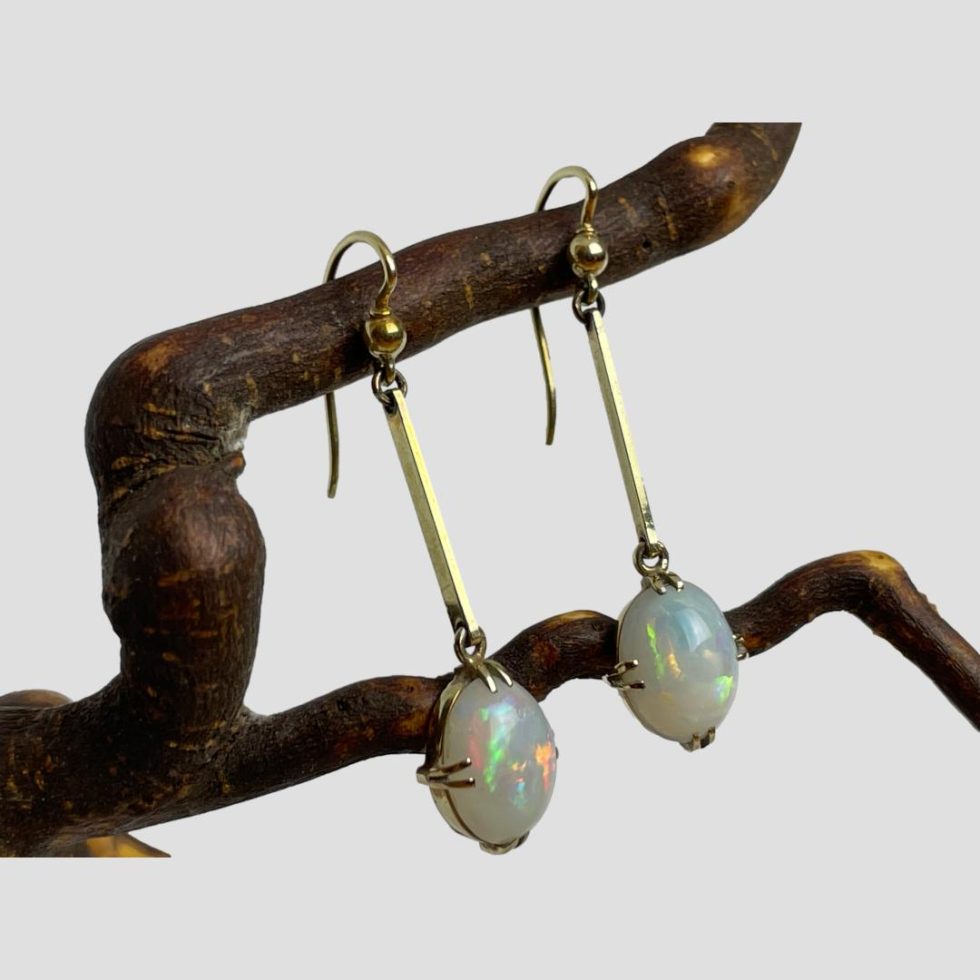 Photo of antique gold opal earrings displayed from a twig of natural wood this time showing them from a slight side angle with the earring fronts facing to the bottom right.