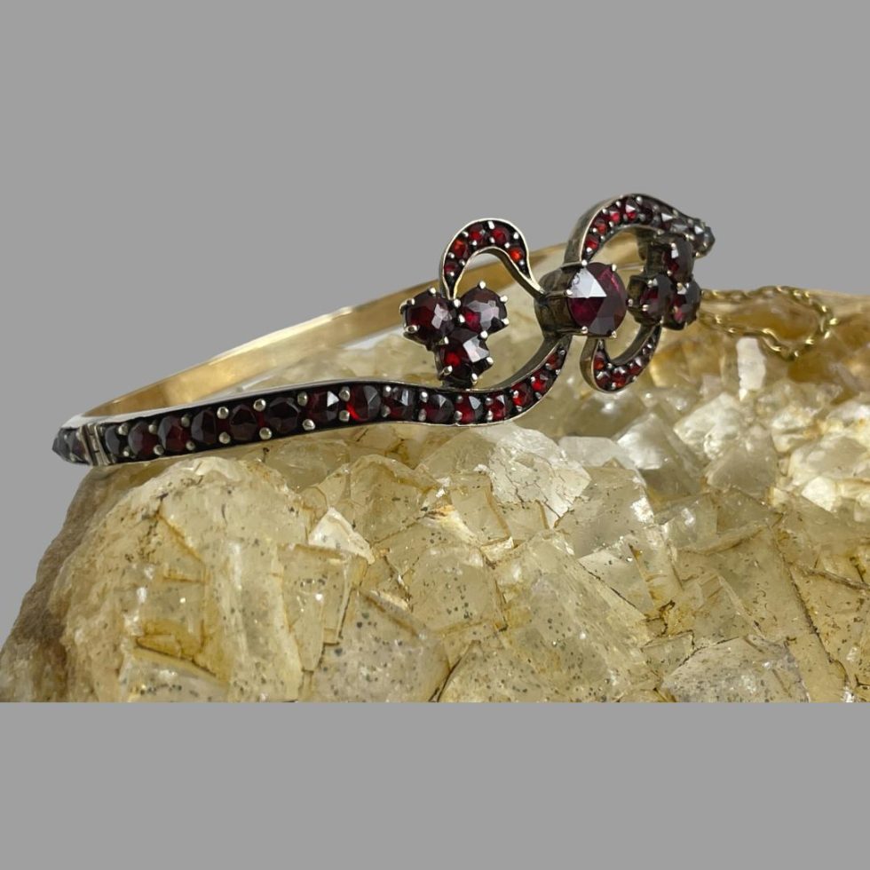Photo of antique garnet bracelet still displayed on a rock of natural river quartz this time with the front of the bracelet facing towards the studio light on the right. The garnets are a gorgeous deep red colour.