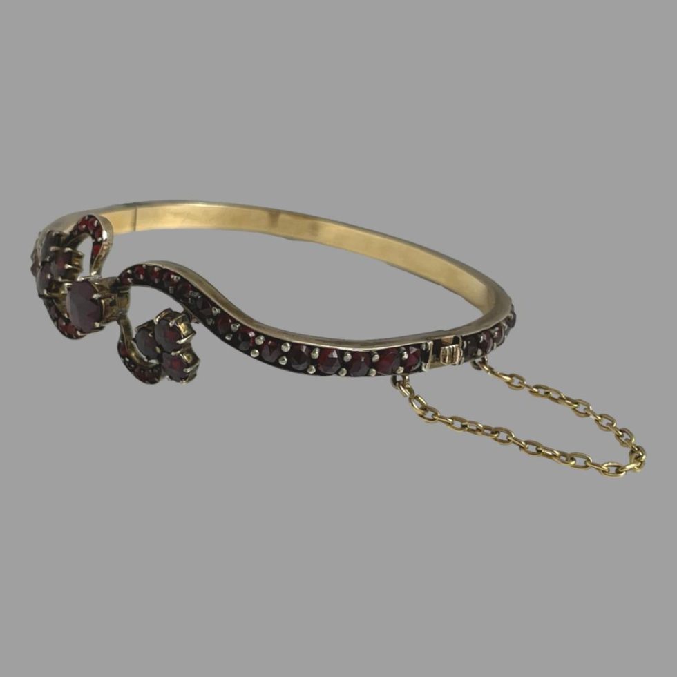Photo of antique garnet bracelet shown laid on a flat surface with the bracelet front facing towards the left. The clasp is on the bottom right with safety chain extended out.