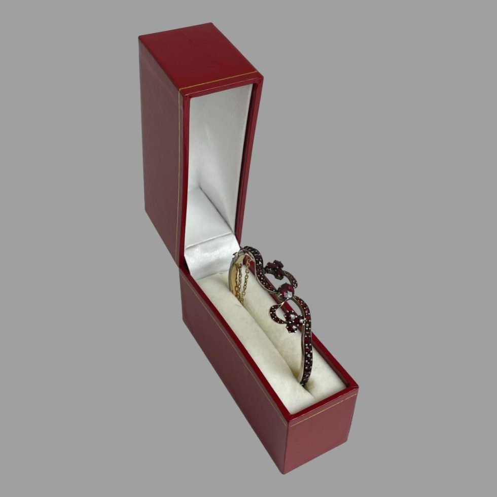 Photo of antique garnet bracelet displayed inside its red box with cream interior. The main bow area of the bracelet is displayed at the top,