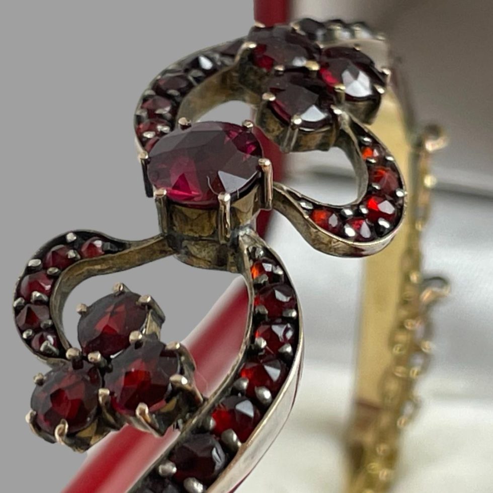 A very close up photo of the bow like front of the antique garnet bracelet which is shown displayed inside its box.