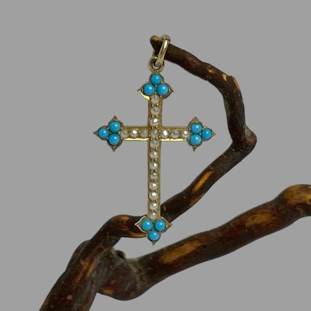 Main photo of antique 18 karat gold cross displayed hanging from a twig of natural cherry wood. The cross is forward facing. The 4 tips of the cross has 3 pointed tips housing 3 small beautiful turquoise blue Sleeping Beauty stones. One stone to pointed tip and 2 immediately behind. 18 seed pearls adorn the rest of the cross. A very pretty piece c1880.