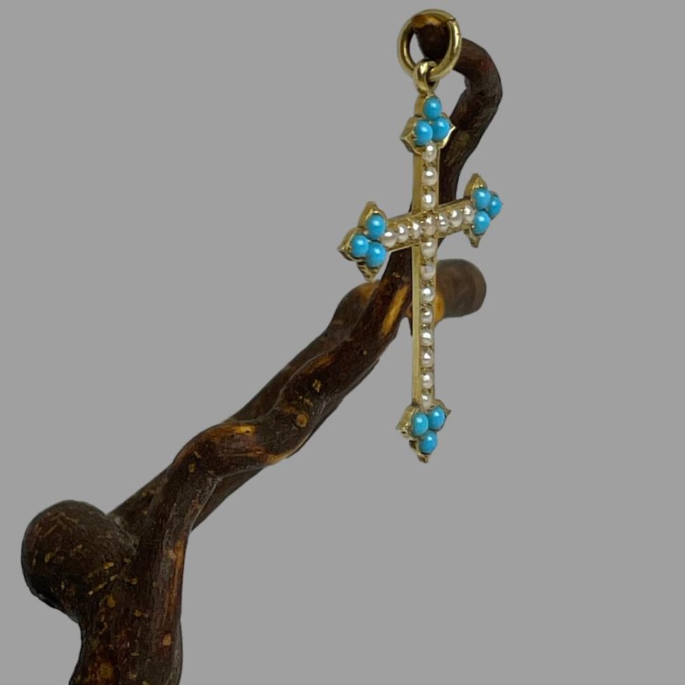 Photo of antique 18karat gold cross c1880 still displayed hanging from a twig of natural cherry wood this time seen a little from a side angle with the front of the cross facing towards the bottom right of photo.