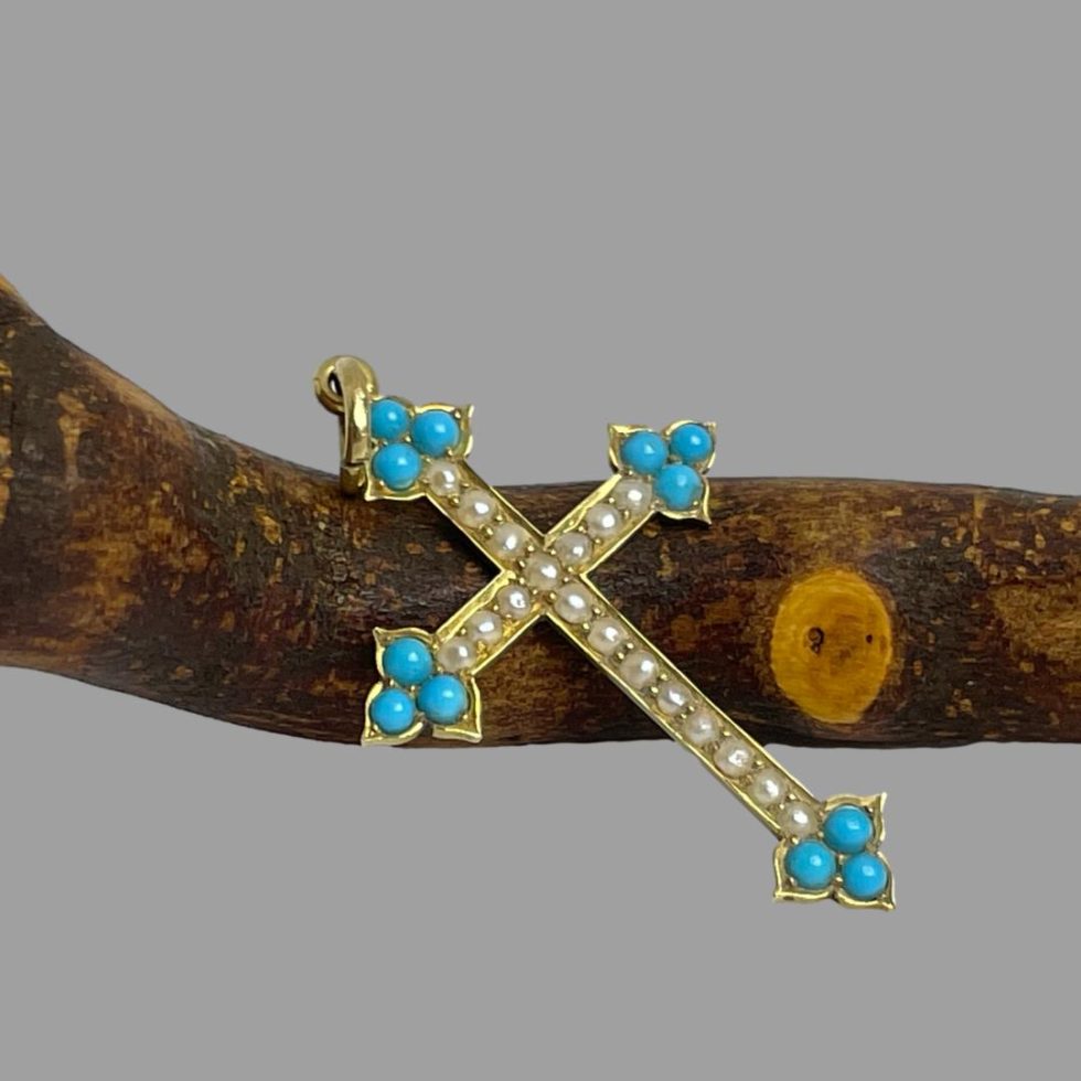 Photo of antique 18 karat gold cross displayed leaning against the cherry wood twig. The cross is laid leaning diagonally with the front facing to upper right.