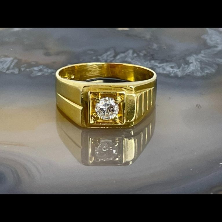 Main photo of gold diamond signet ring displayed on natural agate with the ring front forward facing. This ring is chunky and solid and has an unusual shoulder design. One shoulder has a row of what look like 4 bricks laid side by side whilst the other shoulder is a single groove line. Very distinct design detail.